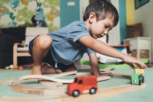 Cute little boy playing with wooden train on the floor at home